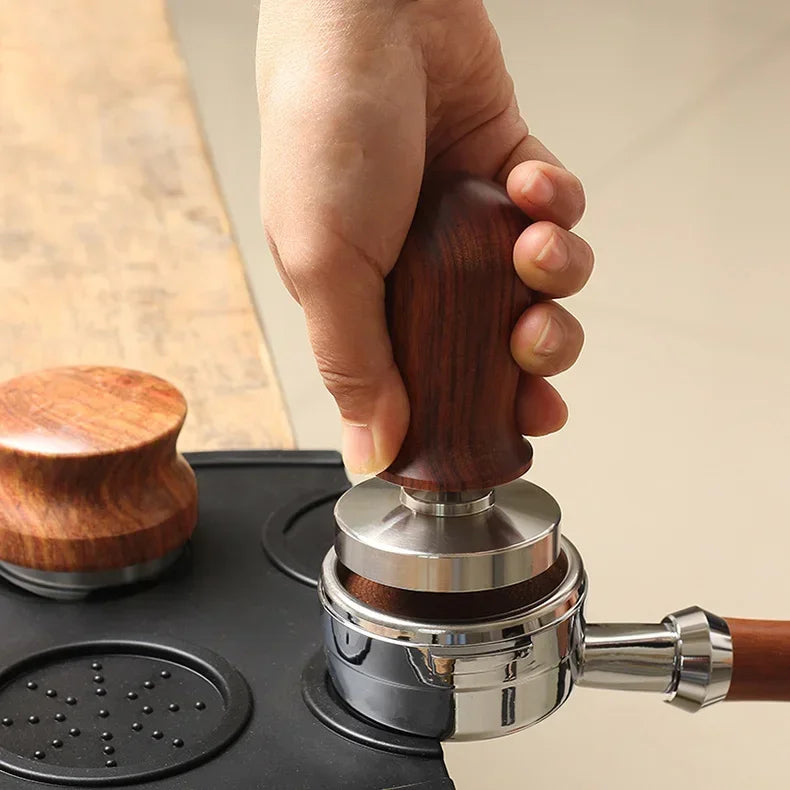 Hand using a wooden coffee tamp to press grounds into a portafilter basket.