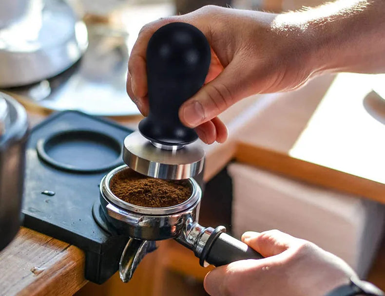 Person using a coffee tamper to compress coffee grounds in a portafilter.
