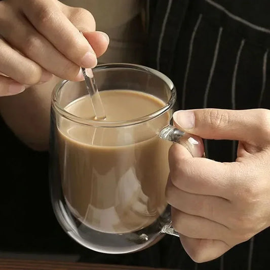 Person stirring a double wall glass cup of coffee with a spoon